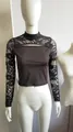 Detalle de un top corto negro de manga larga con encaje floral y recorte en el frente - S / Tops / Negro