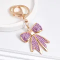 Vue détaillée d'un porte-clés en forme de nœud doré orné de strass violets étincelants - Violet