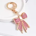 Détail d'un élégant porte-clés doré orné d'un nœud étincelant en strass roses pour sac à main féminin. - Rose