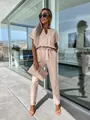 Model wearing an elegant beige V-neck short sleeve jumpsuit with a waist belt and metal detail - S / Jumpsuits / Apricot