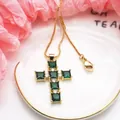 Close-up of golden cross pendant with square green zircons and sparkling clear accents - Necklace / Green
