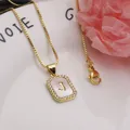 Macro detail of a square gold necklace pendant with white shell inlay and letter J - Letter J