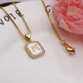 Detailed macro view of square letter M gold pendant with white shell and zircon stone inlay - Letter M