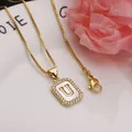 Close-up of a gold square pendant necklace featuring a shell-inlaid letter U - Letter U