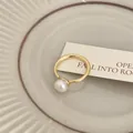 Primo piano di un elegante anello d'oro con una perla bianca su un piatto di ceramica - Stile aperto con perla singola / Oro