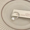 Primo piano di un anello aperto in argento con una perla bianca lucida e raffinata. - Stile aperto con perla singola / Argento