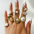 Main portant un ensemble de bagues géométriques dorées avec des perles pour un look chic - Style Perle Artificielle Géométrique Vintage de 8 Pièces (33458-ring-G)