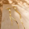 Close-up of golden long tassel earrings with flat snake chains on stone background - Gold