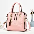 Elegante rosa Lackleder-Handtasche mit Krokodilprägung und dekorativem Katzenanhänger. - Hellrosa