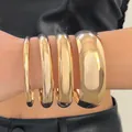 Detailed view of four high-polished gold chunky bangles in varying widths on arm - 4 Pieces Collection (Set)