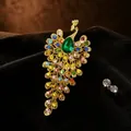 Detalle macro de un broche de pavo real estilo vintage con pedrería de colores y piedra verde. - Broche de Pavo Real / Oro esmeralda