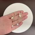 Elegante goldfarbene Tulpen-Ohrhänger mit weißen Perlen, auf der Hand präsentiert. - Weiß