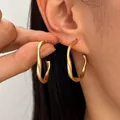 Minimalist matte gold twisted geometric hoop earrings displayed on an Asian model's ear - Twisted Geometric Style / Matte Gold