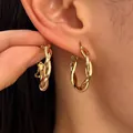 Elegant and minimalist gold-finish twisted hoop earrings shown as worn on an ear model. - Triple Strand Twist Style / KC Gold