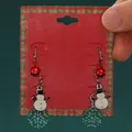 Festive Christmas snowman and snowflake drop earrings displayed on a red gift card - Bell Snowman Snowflake Set (H-148)