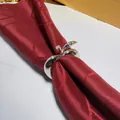 Detailed shot of a silver apple-shaped napkin ring on a red textured napkin. - White K/Silver