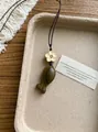 Gros plan d'un pendentif en bois en forme de poisson avec une petite perle florale - Couleur Bois de Santal Vert / Café Clair