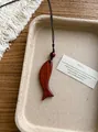 Détail d'un collier pendentif en bois en forme de poisson sur un plateau minimaliste - Poisson Courbé / Café Foncé