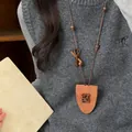Detailansicht einer modischen Brillenclip-Halskette aus Leder mit Bär auf einem grauen Pullover. - Teddybär / Kaffeebraun