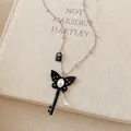 Detailed close-up of a black butterfly key necklace with crystal drops on a linen book - Butterfly Key Style / Silver Black Butterfly