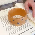 Ethno-Armreif aus orangefarbenem Holz mit silbernen Metallnieten auf einem Buch - Khaki