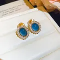 Detail view of oval blue resin stud earrings with delicate pearl border on white display - Clip-On Earrings / Blue