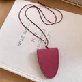 Detailed view of a minimalist maroon leather glasses holder necklace on a fabric book. - Shield Shape / Red