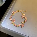 Detail shot of a gold-toned bracelet with pink leaf crystals and rhinestone flowers - Bracelet / Gold-Pink