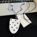 Detailed view of a stylish white polka dot leather glasses case pendant necklace on a desk - White