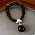 Close-up van een meerrijige zwarte kralenketting met een grote bolvormige hanger. - Zilver-Zwart