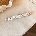 Detail van een witte geplooide stoffen haarspeld met zwarte stippen op een linnen achtergrond. - Zilveren metalen label decoratie / Veerclip - Wit