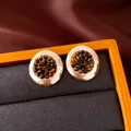 Vista macro de elegantes pendientes redondos dorados vintage con piedras oscuras - Diseño Plisado Redondo / Marrón dorado
