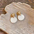 Boucles d'oreilles dorées avec disques blancs texturés présentées sur un plateau en céramique. - Style Géométrique Irrégulier (HE35514) / Or+Blanc