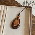 Primer plano detallado de un colgante ovalado de resina retro de doble capa con cordón tejido marrón - Estilo de Elipse Anidada