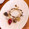Detailansicht eines vintage doppelreihigen Armbands mit Erdbeer Herz Anhängern und Perlen - Doppelschichtige Erdbeerschleife Stil / Gold Mehrfarbig
