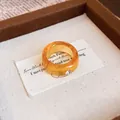 Nahaufnahme eines bernsteinfarbenen Harzrings mit kleinem Diamanten auf weißem Stoffdekor - Runder Schuppenring / Braun