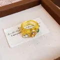 Nahaufnahme eines gelben Harzrings mit bunten Edelsteinen auf Stoff - Runder Schuppenring / Gelb-Kaffee