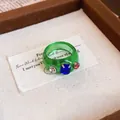 Detailansicht eines grünen Harzrings mit eingelegten blauen, roten und weißen Kristallen. - Runder Schuppenring / Grün - Blau