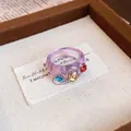 Detailansicht eines lila Harzrings mit drei bunten eingebetteten Strasssteinen heute - Runder Schuppenring / Lila Und Braun