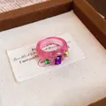 Detailaufnahme eines rosa Harzrings mit lila, grünen und gelben Kristallen für Damen - Runder Schuppenring / Rosa-Lila