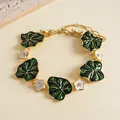 Detailed view of vintage green leaf and white flower charms on a gold bracelet - Gold-Green