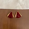 Primer plano detallado de pendientes triangulares de esmalte rojo con bordes dorados - Triángulo Dorado / Rojo