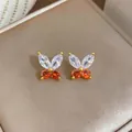 Detailansicht von Schmetterlingssteckern mit weißen und orangefarbenen Steinen - Gold-Rot