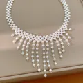 Detalle del elegante collar con flecos de perlas blancas sobre una base de color beige. - Blanco