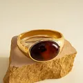 Nahaufnahme eines goldenen Metallarmbands mit großer dunkelbernsteinfarbener ovaler Harzeinlage - Gold-Kaffee