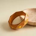 Detailansicht eines Vintage-Harzarmreifens mit Holzmaserung und goldenen Nieten - Beige