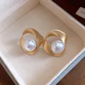 Macro-weergave van elegante geometrische goudkleurige oorknopjes met grote witte parels - Goud