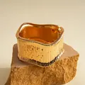 Detailansicht eines goldenen Vintage-Armreifs mit strukturierter Oberfläche auf Fels - Öko-Gold