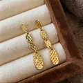 Detalle de pendientes colgantes ovalados de metal martillado dorado con textura. - Dorado