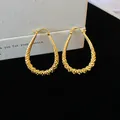 Close-up of gold finish geometric waterdrop hoop earrings with intricate textured details. - Gold